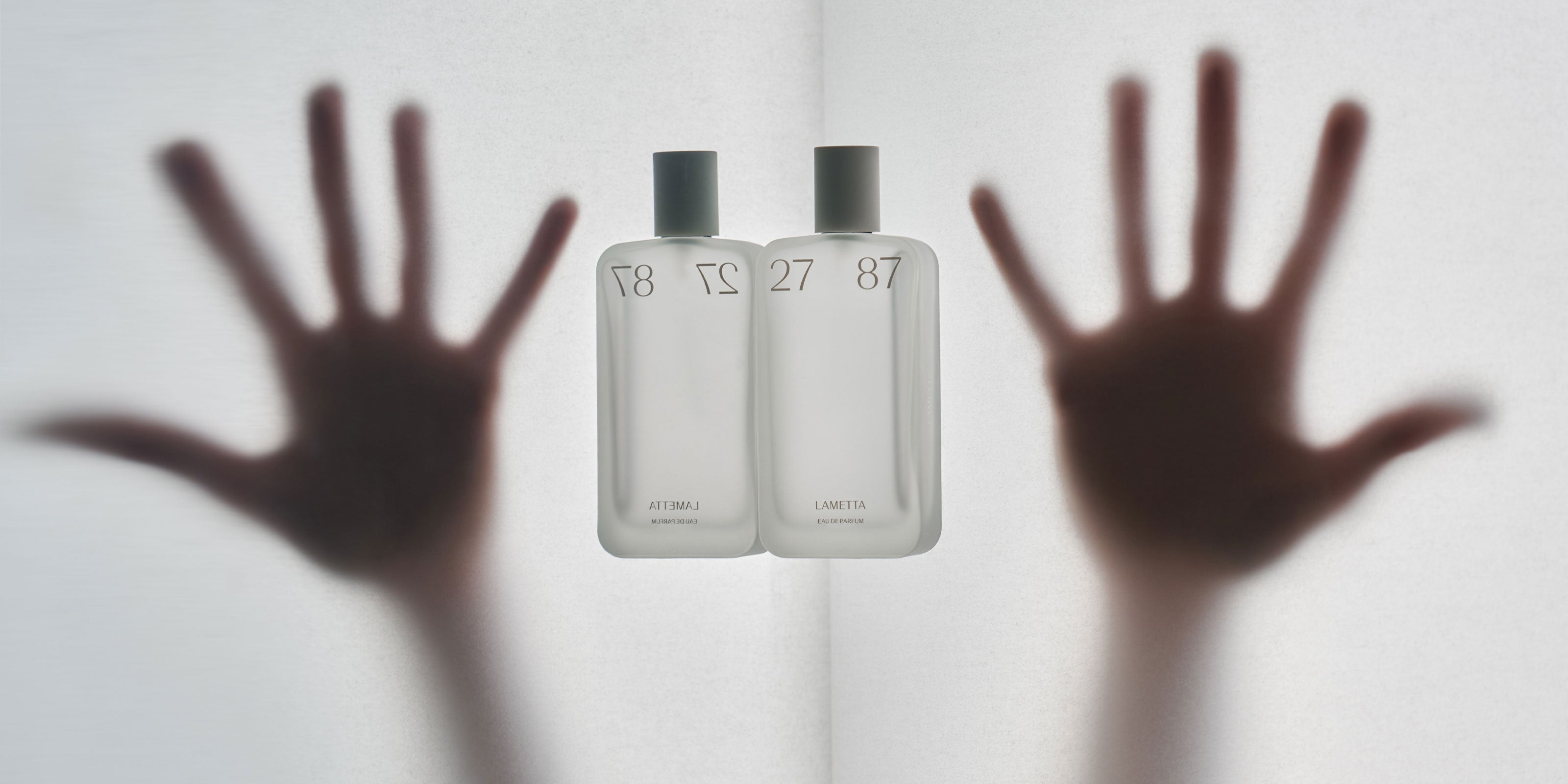 Parfumflakon mit zwei Händen im Hintergrund