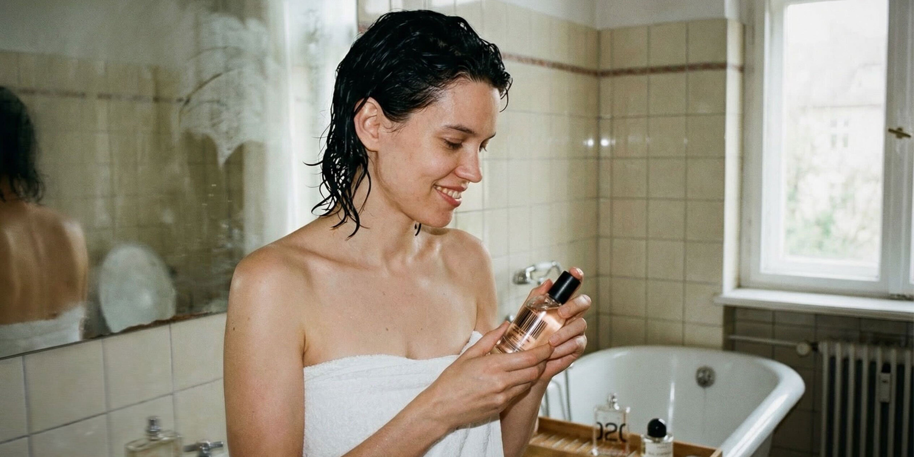 Frau in Handtuch eingewickelt die einen Flakon in der Hand hält